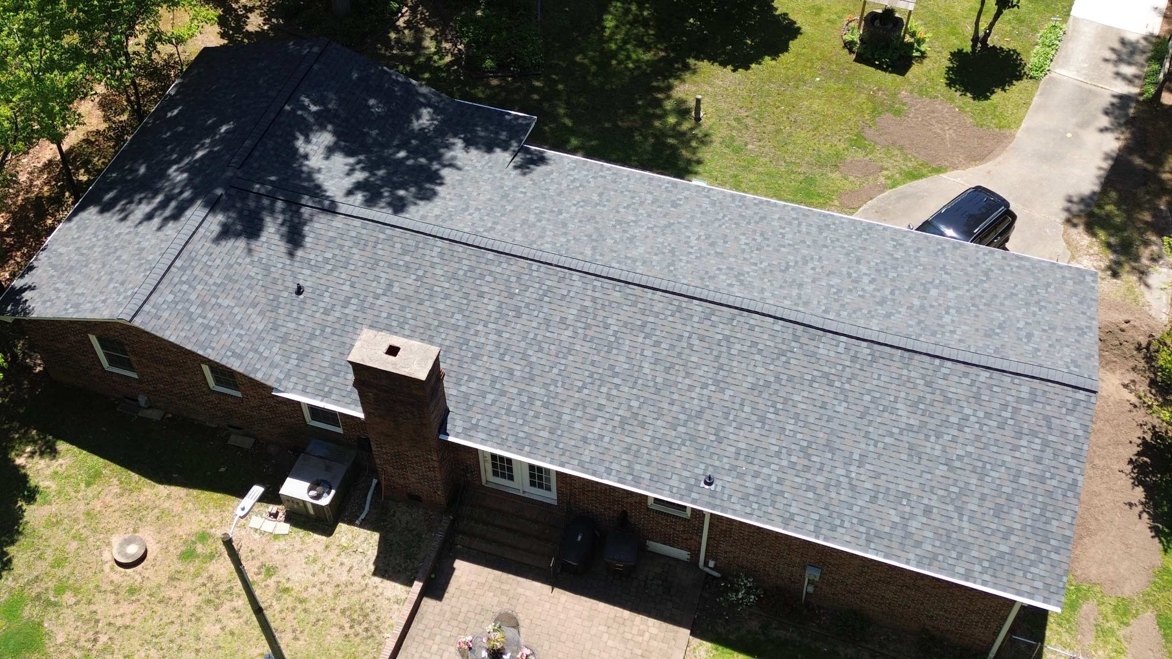 Drone view of a long brick ranch house with a new gray shingle roof.