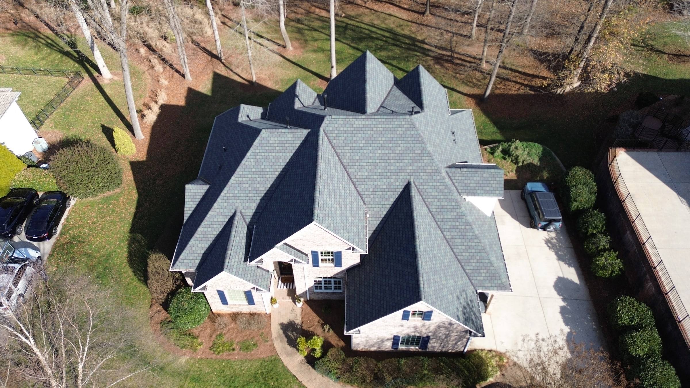 Drone view of a finished Escalade roof: a steep roof with many gables and valleys over a brick home.