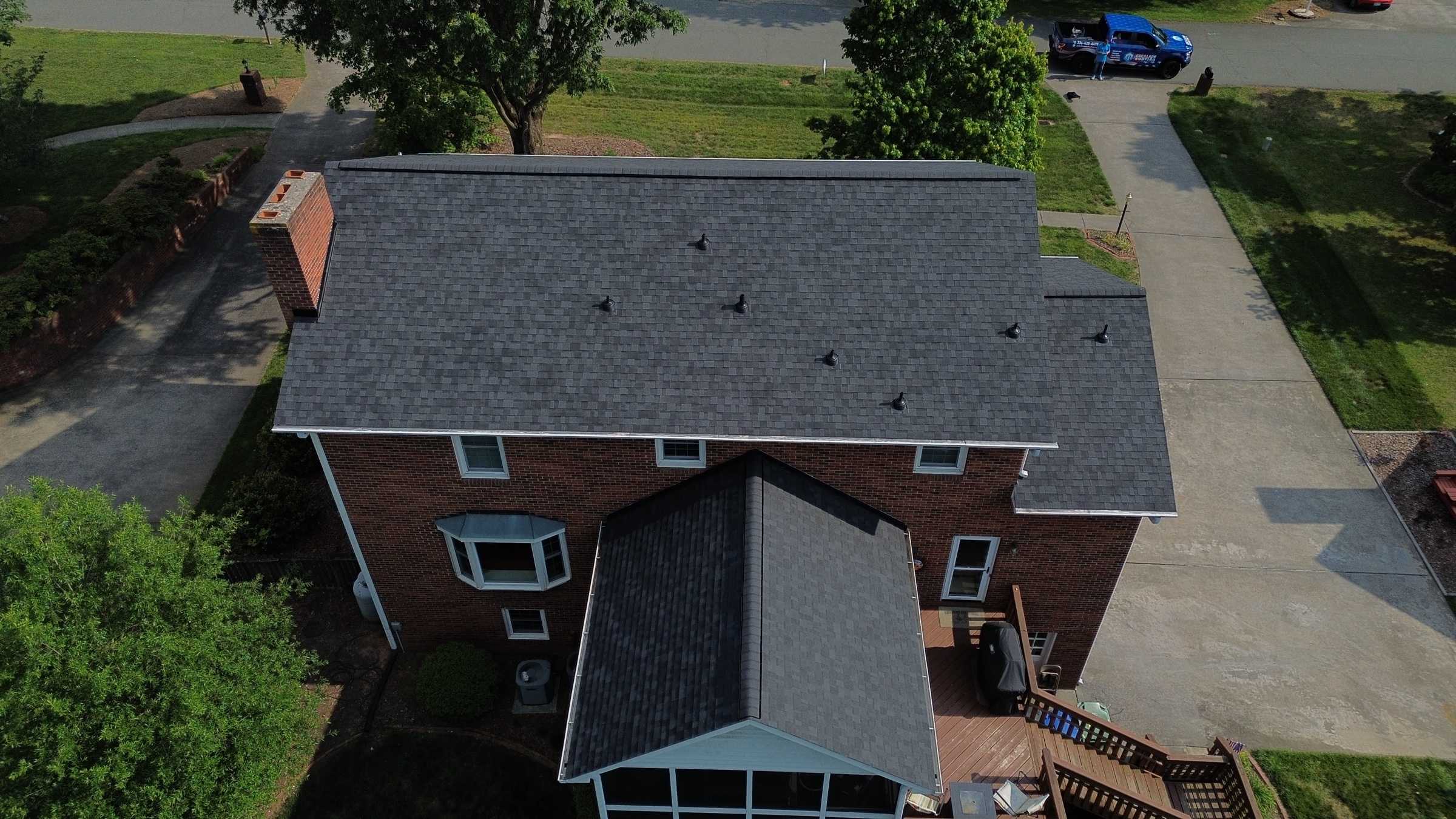 Drone view of a brick two-story house with a new dark gray shingle roof and a screened porch.