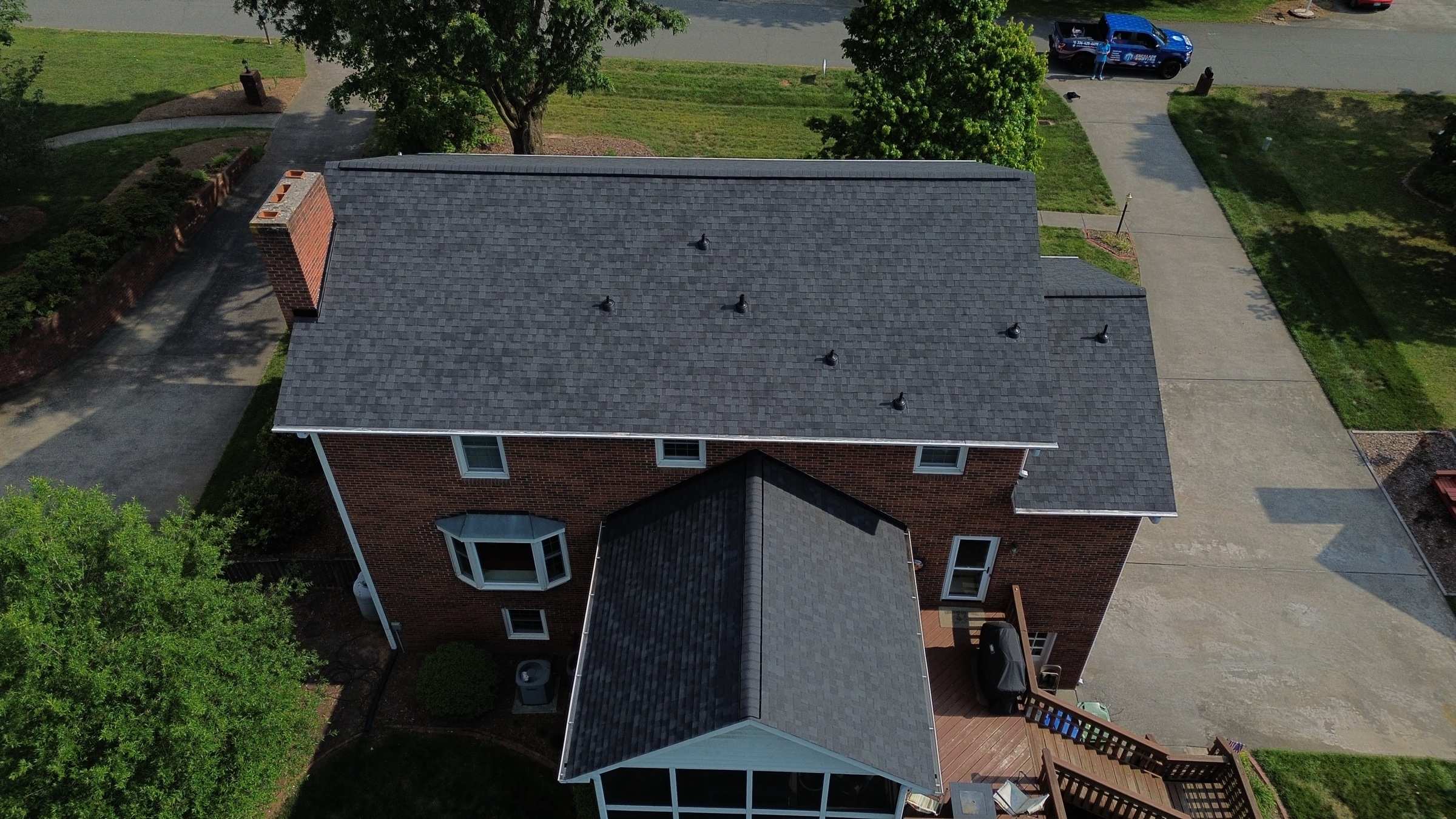 Drone view of a brick two-story house with a new dark gray shingle roof and a screened porch.